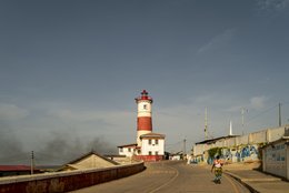 Lighthouse,-Coastal-road,-Street-life,-Passers-by,-Smoke,-Mural,-Street-art,-British-colonial-architecture,-Victorian-era,-Working-class-neighbourhood,-Golden-light,-Jamestown,-Accra,-Ghana,-West-Africa